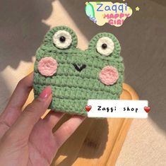 a hand holding up a green crocheted cell phone case with two googly eyes