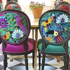 two chairs with colorful designs on them sitting in front of a table and potted plant