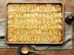 a pan filled with baked potatoes on top of a wooden table next to a spoon