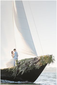 a bride and groom standing on the back of a sailboat in the ocean with greenery