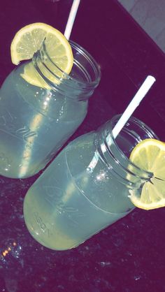 two mason jars filled with lemonade and topped with straws on a black counter