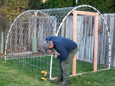 a man bending over to pick up something from the ground in front of a garden trellis