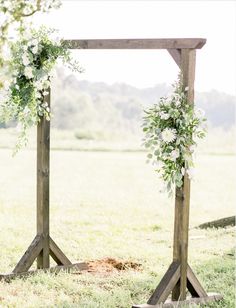 an outdoor ceremony setup with flowers and greenery on the top of wooden poles, in front of a grassy field