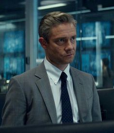 a man in a suit and tie sitting at a desk with his head turned to the side