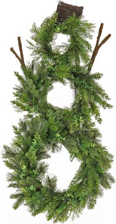 a christmas wreath with pine branches and evergreens on the front, hanging from a white wall