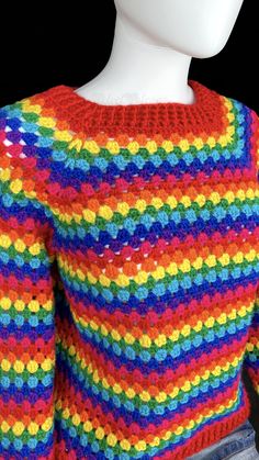 a white mannequin wearing a multicolored knitted sweater on a black background