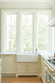 a kitchen with white cabinets and wood floors is pictured in this image, there are two windows above the sink