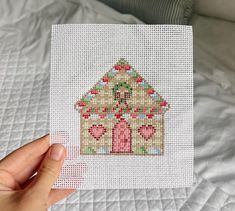 someone is holding up a cross - stitch picture of a gingerbread house on a bed