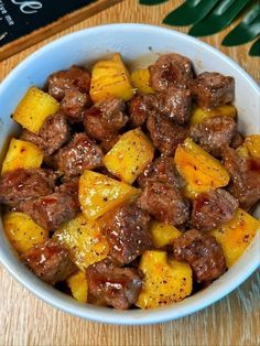 a white bowl filled with meat and pineapples on top of a wooden table