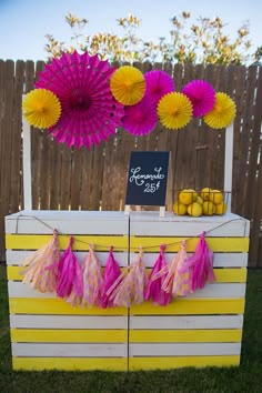 a yellow and white table topped with pink tissue pom poms next to a fence