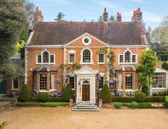 a large brick house with lots of windows and bushes around the front door, on a sunny day