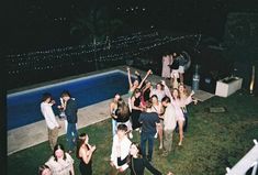 a group of people standing around each other in the grass near a pool at night