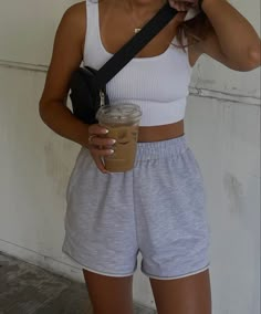 a woman in shorts and tank top holding a cup of coffee while talking on a cell phone