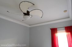 the ceiling fan is hanging from the ceiling in the room with red drapes on the windowsill