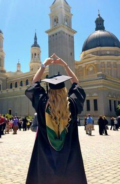 a woman wearing a graduation gown and cap standing in front of a building with a clock tower