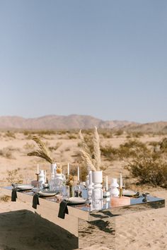 an outdoor table set up in the desert with white candles and black napkins on it