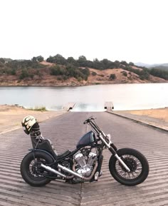 a motorcycle parked on the side of a road next to a body of water with trees in the background