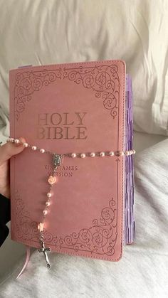 a hand holding a pink bible with beads on it