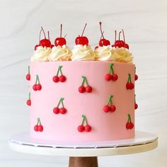 a pink cake with cherries and white frosting on a stand next to a wall