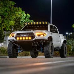 the white truck is parked on the side of the road at night with its lights on