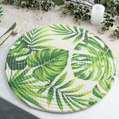 a place mat with green leaves on it next to silverware and candlesticks