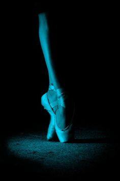 a ballerina's feet are lit up in the dark with blue lighting on them