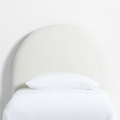 a bed with white sheets and pillows on it's headboard in front of a wall