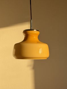 a yellow light hanging from a ceiling in a room with white walls and shadows on the wall