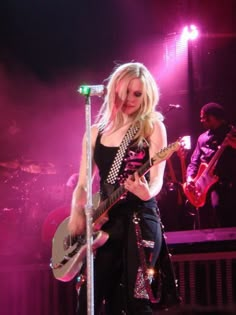 a woman holding a guitar on top of a stage