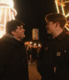 two young men standing next to each other in front of a ferris wheel at night