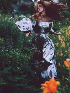 a woman in a silver dress is running through the grass with her hair blowing in the wind