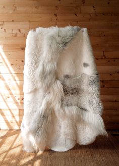 a white and grey fur blanket sitting on top of a wooden floor next to a wall