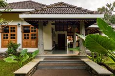 a white house with wooden doors and steps leading up to the front door is surrounded by lush greenery