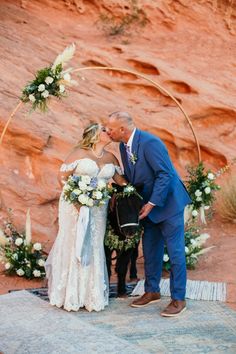 a bride and groom kissing in front of a rock arch at their desert wedding ceremony