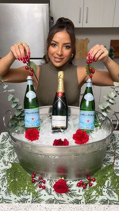 a woman sitting at a table with three bottles of wine in front of her and two roses on the table