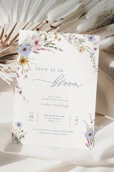 a white card with flowers and feathers on it that says, love is in bloom