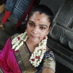 a woman in a pink sari with flowers around her neck posing for the camera