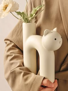 a person holding a vase with a flower in it and a cat figure on the side