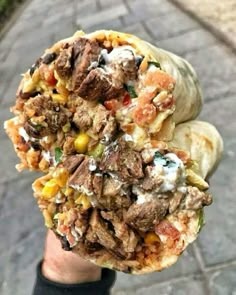 a person holding up a burrito filled with meat and veggies on it