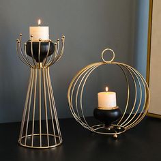 two candles are sitting on a table next to a wire holder with a candle in it