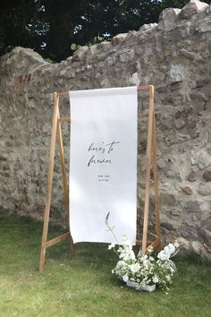 a white sign sitting on top of a grass covered field next to a stone wall