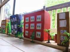 a row of cardboard houses sitting on top of a window sill next to a tree