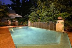 an empty swimming pool in the middle of a garden at night with lights on and umbrella over it