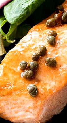 a piece of meat sitting on top of a black plate next to spinach leaves