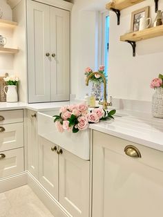 a kitchen with white cabinets and pink flowers on the counter