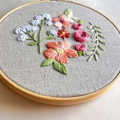 a close up of a embroidery on a hoop with flowers in the center and leaves