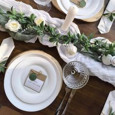 the table is set with white plates, silverware and greenery for an elegant look