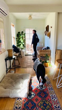 two people standing in a living room with a dog on the rug and another person looking at them