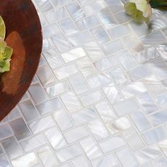 a vase filled with flowers sitting on top of a white tiled floor next to green leaves