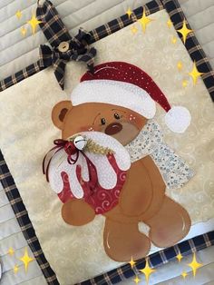 a teddy bear wearing a santa hat and holding a christmas ornament on a quilt